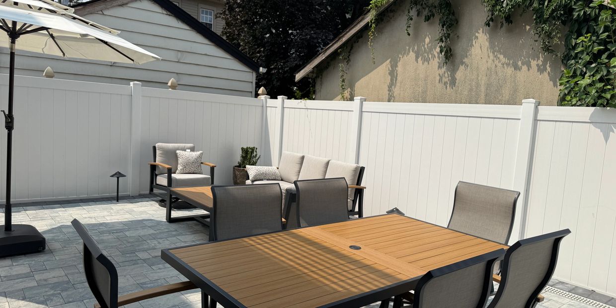 Modern outdoor patio with wooden furniture and white fencing under clear skies.