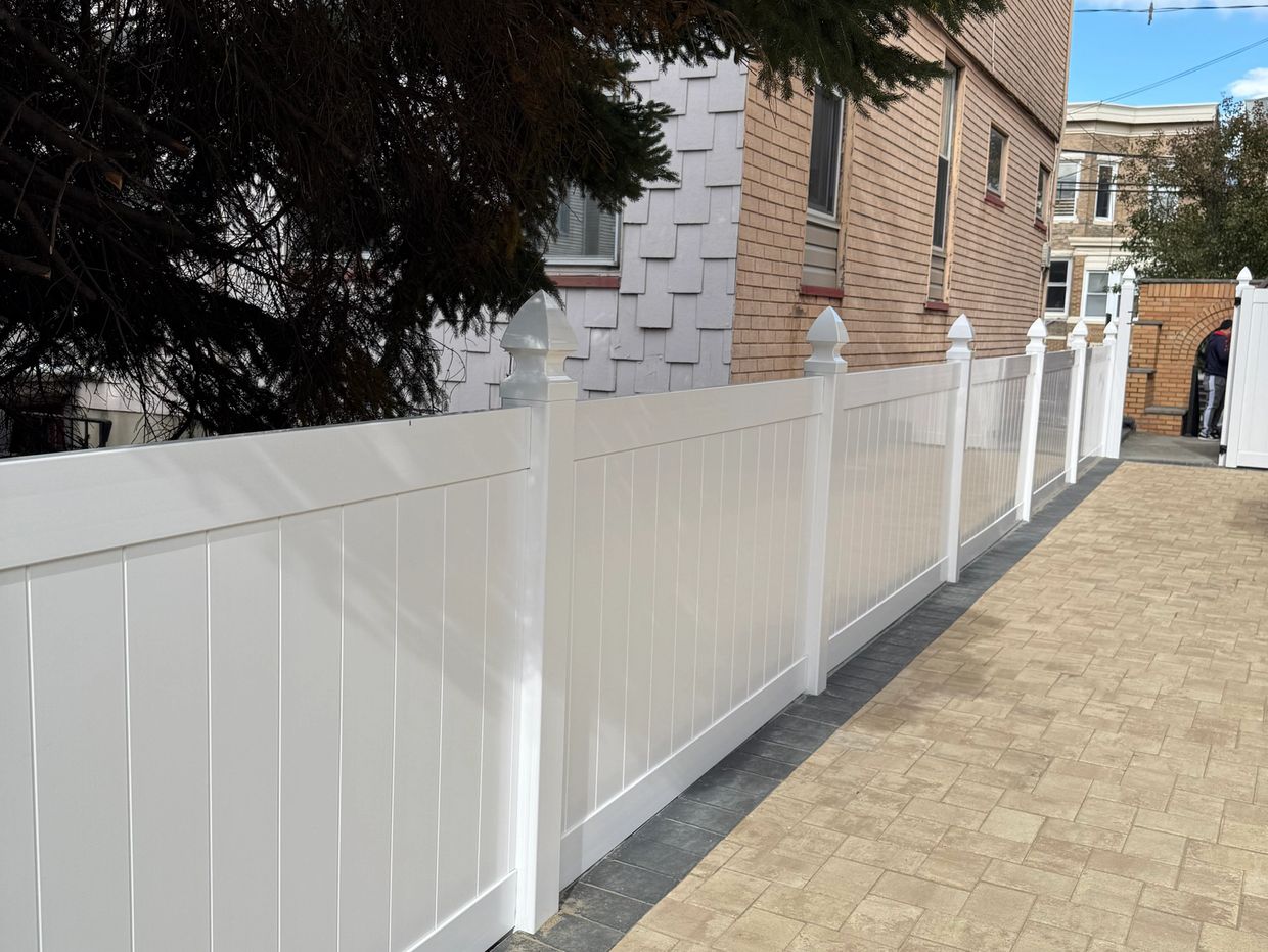 A clean white fence along a paved pathway beside houses. Vinyl Fencing installation