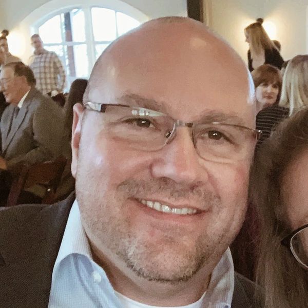 Smiling bald man with glasses at a social gathering indoors.