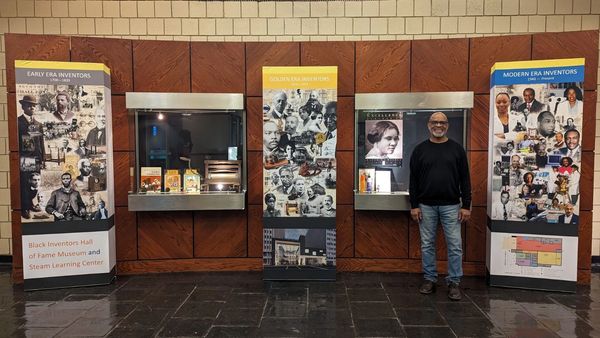 Man standing next to Black inventors exhibit at a museum.