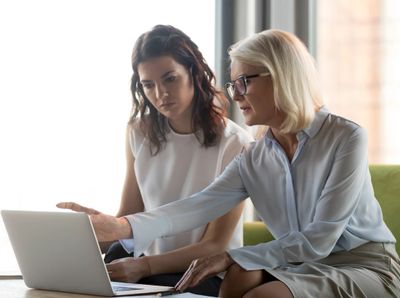 Two women looking at a laptop closely.