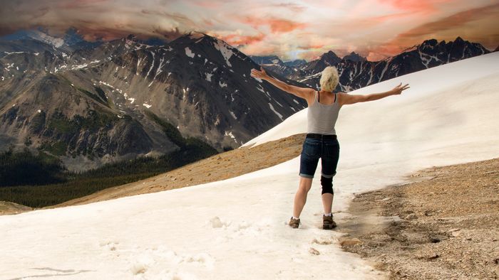A person stands with arms wide open on a snowy mountain slope at sunset.