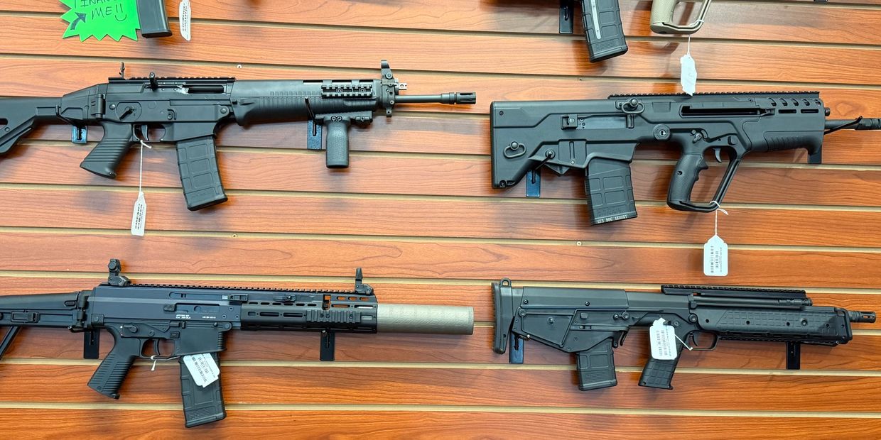 Four black tactical rifles displayed on a wooden wall panel.