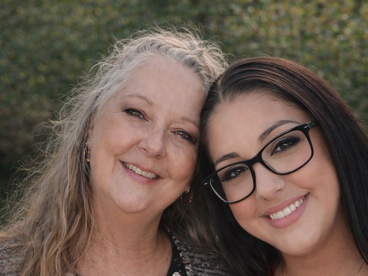 Two women smiling closely together outdoors with a green background.