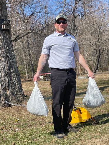 Man outdoors holding two white bags, wearing sunglasses and a cap.