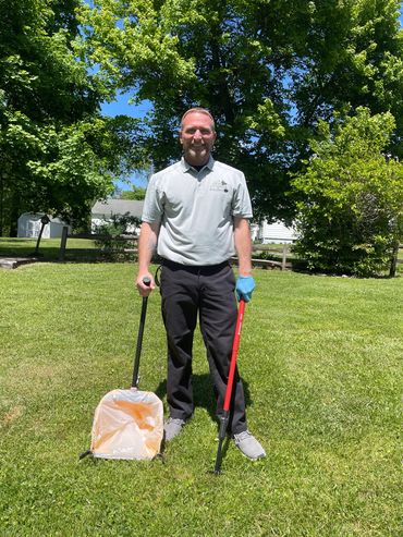Man standing on grass holding litter grabbers and a trash bag.
