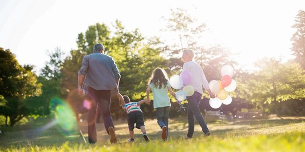 Family of four walking outdoors with balloons on a sunny day.