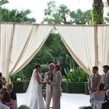 Outdoor wedding ceremony with couple exchanging vows under white drapes.