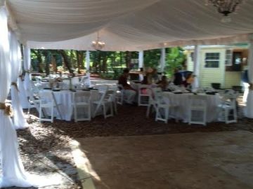 Outdoor event setup with white tables and chairs under a tent.