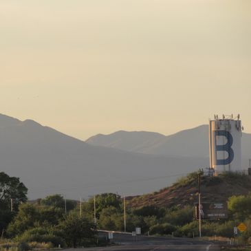 Large water tower with a blue 'B' near mountains at sunset.