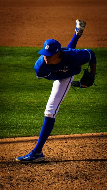 Baseball pitcher in blue uniform mid-pitch on a sunny field.