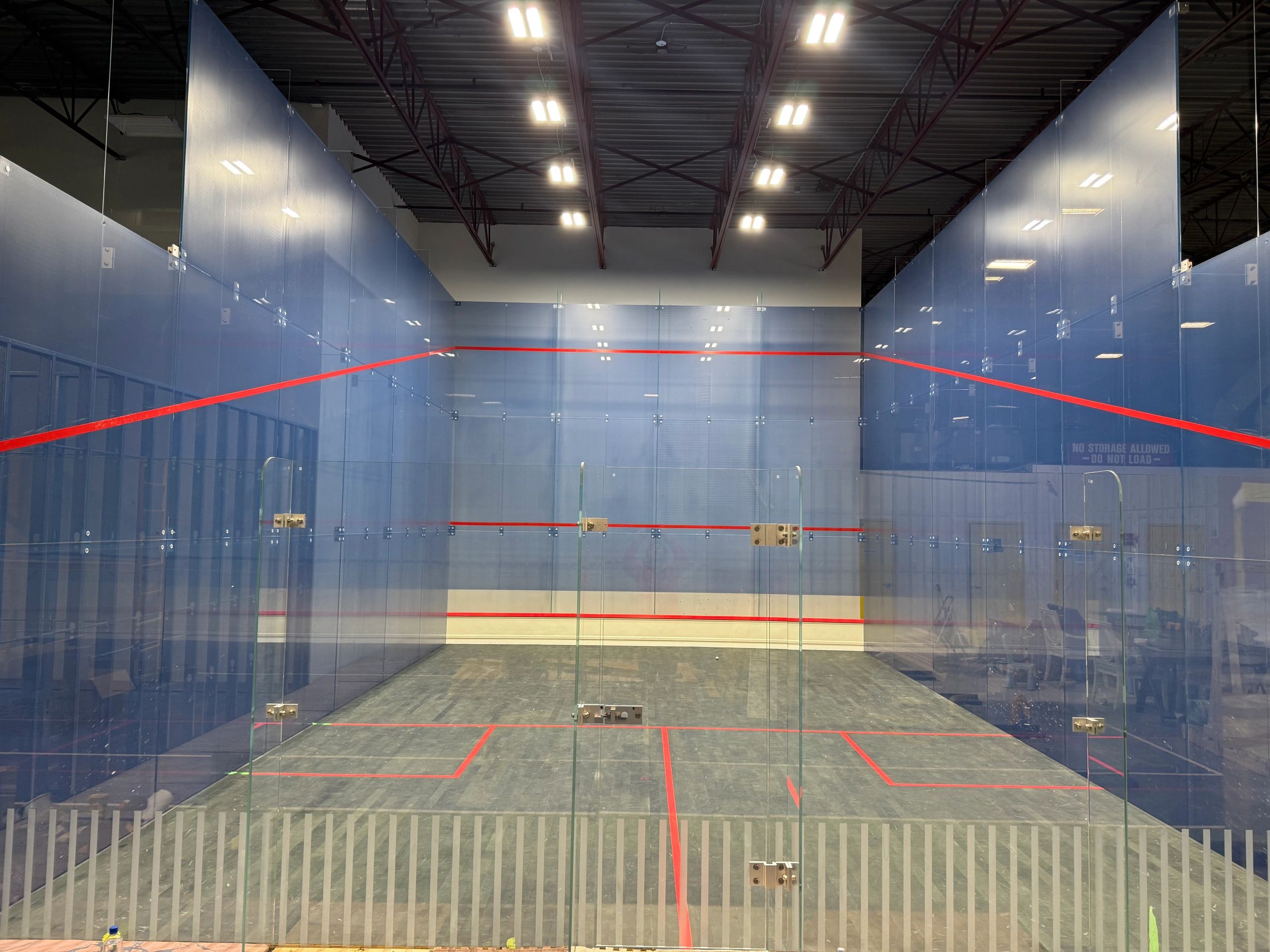 Empty indoor squash court with glass walls and red boundary lines.