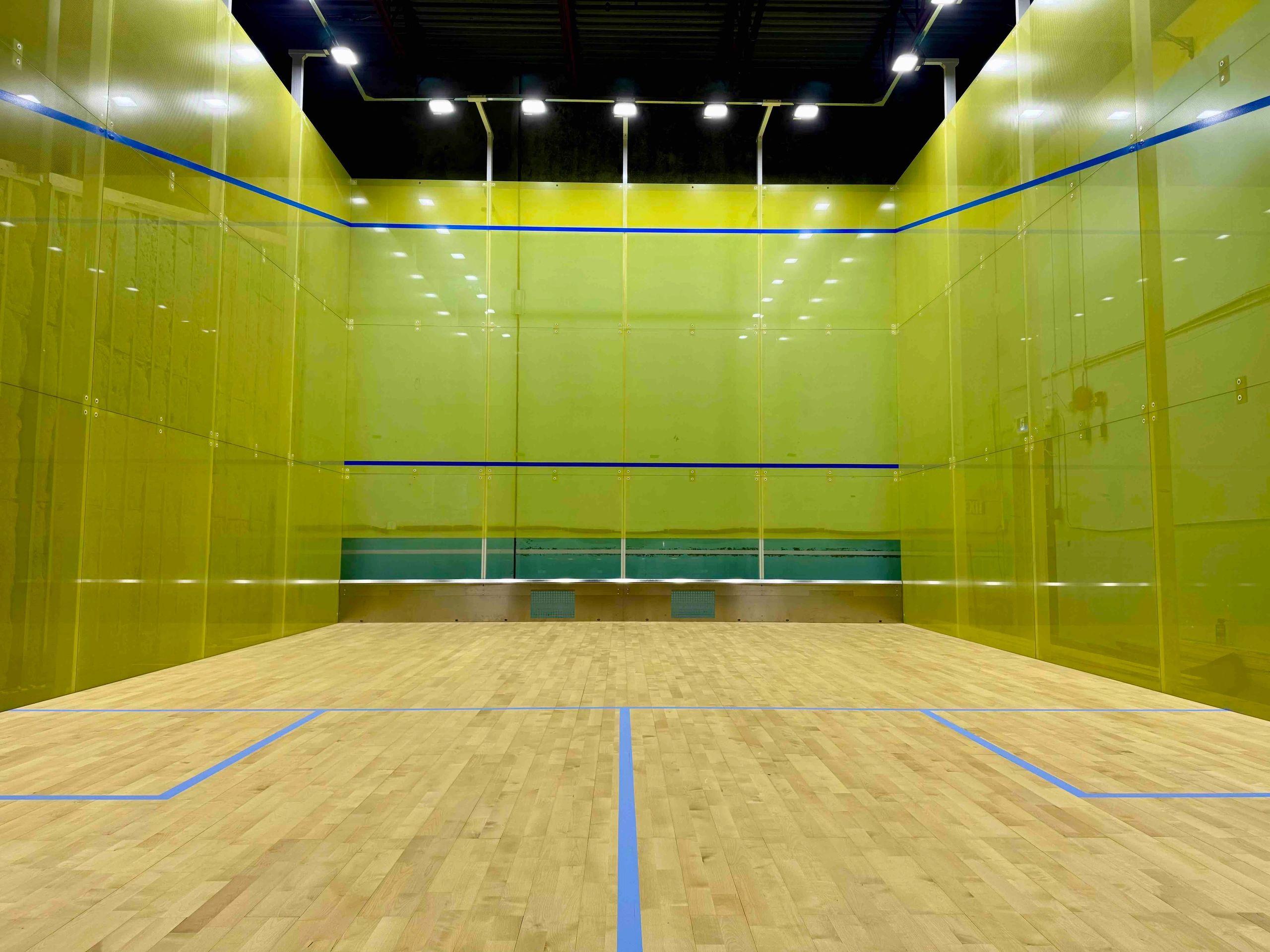 Empty indoor squash court with yellow walls and blue lines.