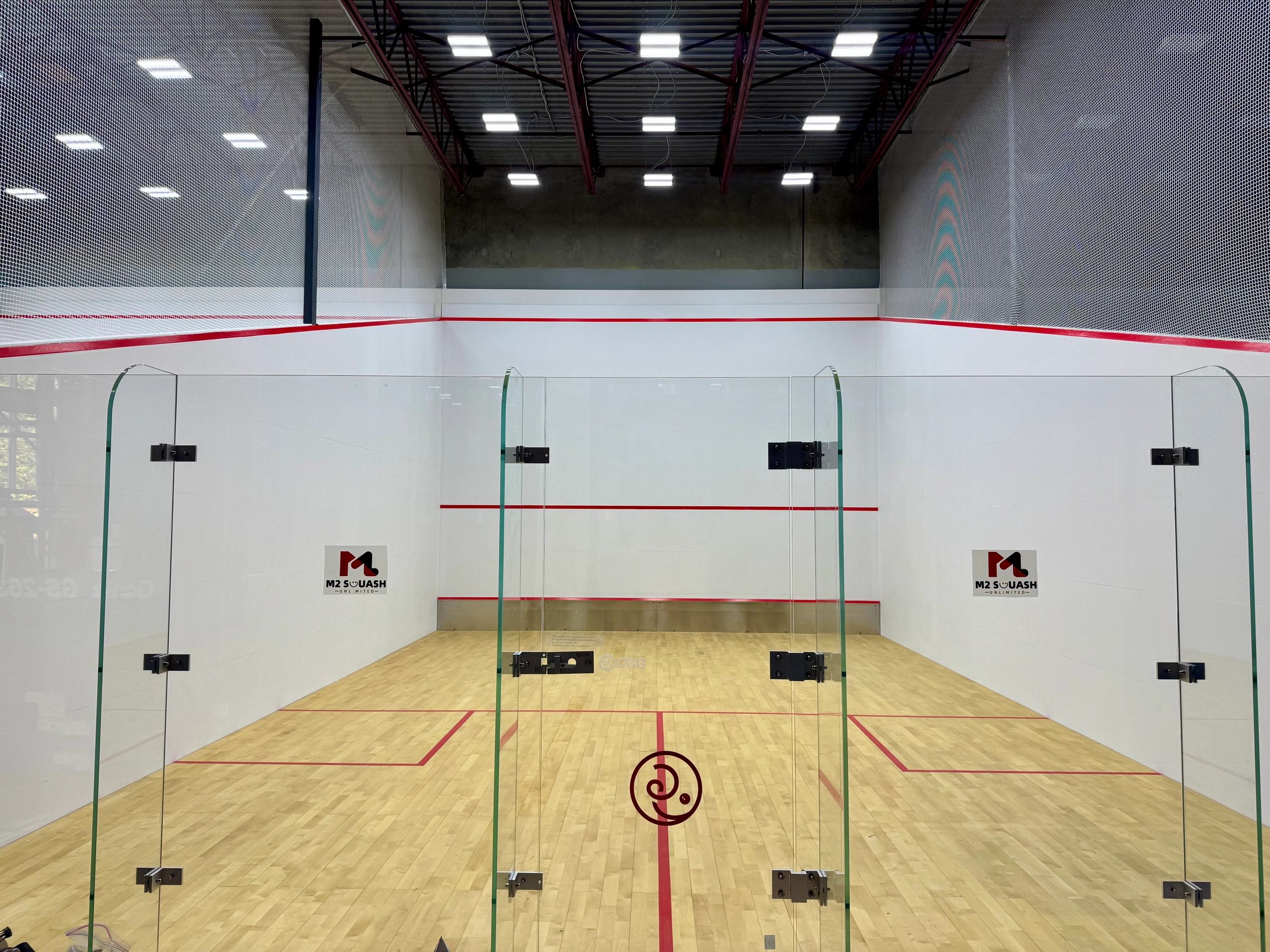 A clean, empty squash court with glass walls and wooden floor.