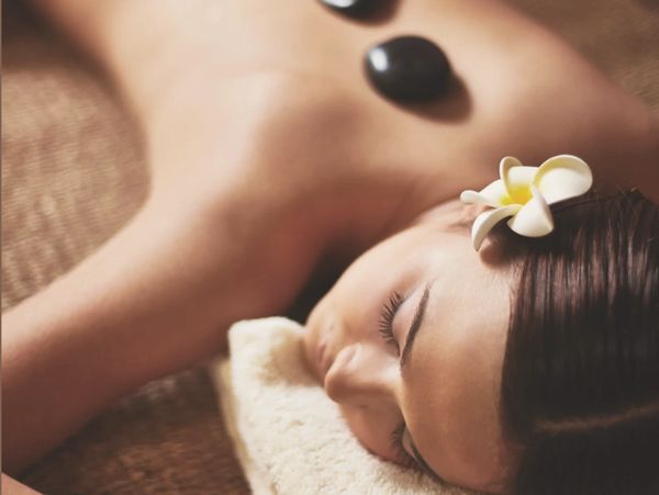 Frau bei Hot-Stone-Massage mit Blume im Haar.