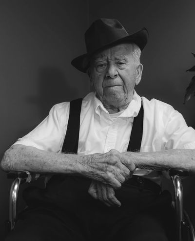 An elderly gentleman seated in a wheelchair, wearing suspenders and fedora.
