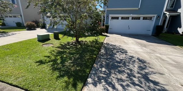 Sunny residential driveway with green lawn and utility boxes.