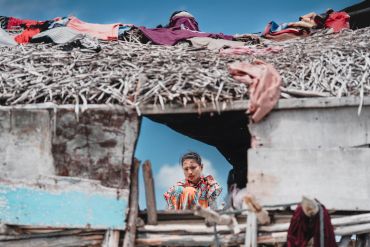 Woman looking through a broken wall of a weathered house.