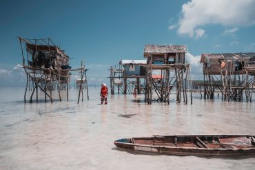 Stilt houses over shallow water with a person and boat.