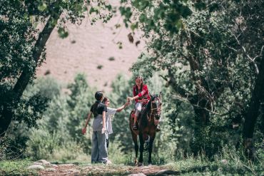 Person on horseback reaching out to another in a forest.