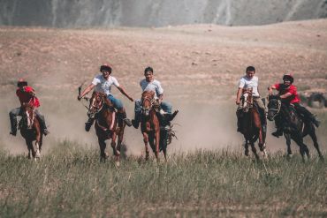 Five riders racing horses across a dusty field.