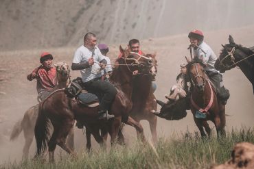 Men engaged in a traditional horse game in a dusty field.