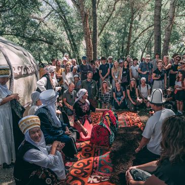 People gathered outdoors around traditional rugs and attire.