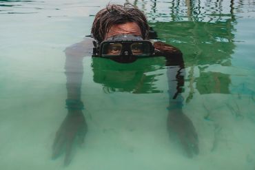 Person snorkeling in clear water wearing goggles.
