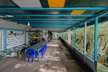 Long walkway with tables and blue chairs in a colorful building.