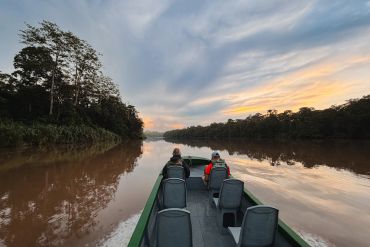 People on a boat in a river during sunset.