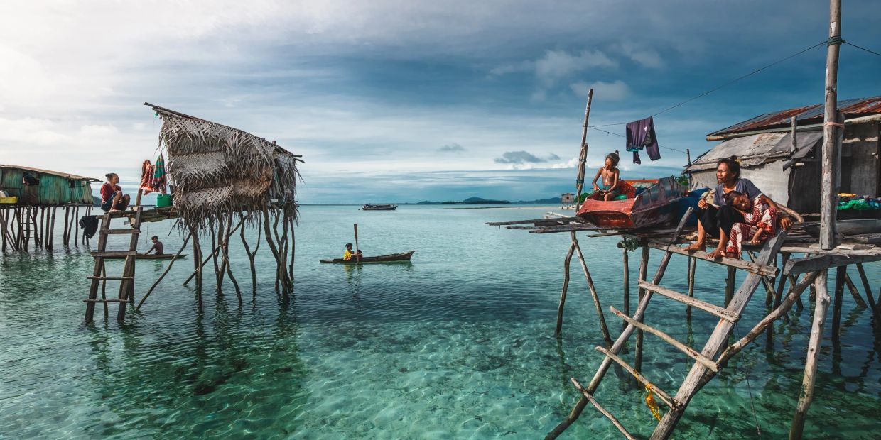 Overwater stilt houses with people by the sea under a cloudy sky.