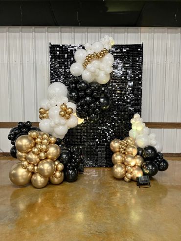 Black, white, and gold balloon arch with a black sequin backdrop.