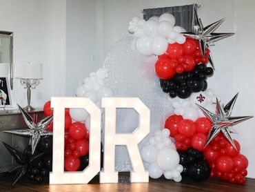 Decorative balloon arch with illuminated letters 'DR' and silver star balloons.