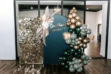 Elegant event backdrop with gold, green balloons, and pampas grass.