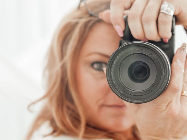 A woman taking a photo with a DSLR camera, focusing on the lens.