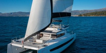A white catamaran sailing on clear blue waters with hills in the background.