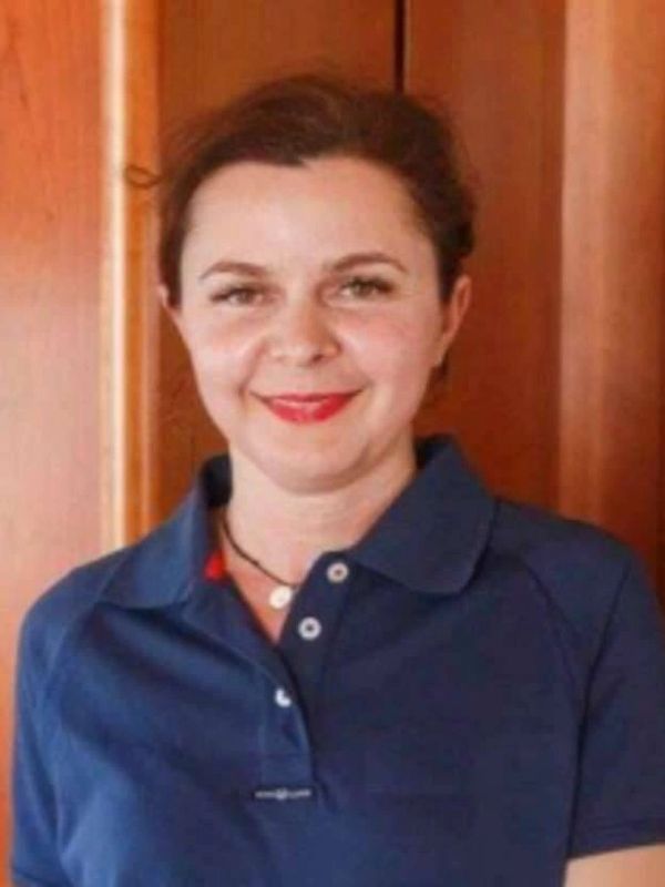 Smiling woman in a navy blue polo shirt standing against a wooden wall.