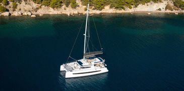 A white catamaran anchored in calm blue waters near a rocky shoreline.