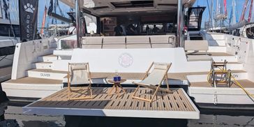 Modern catamaran with deck chairs and a small table, docked at a marina.