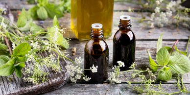 Two amber bottles with essential oils surrounded by fresh herbs on rustic wood.