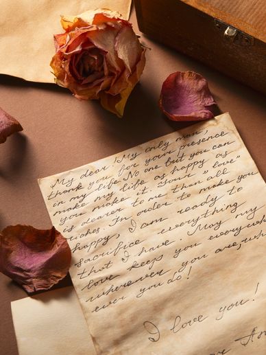 A handwritten love letter surrounded by dried rose petals and a dried rose.