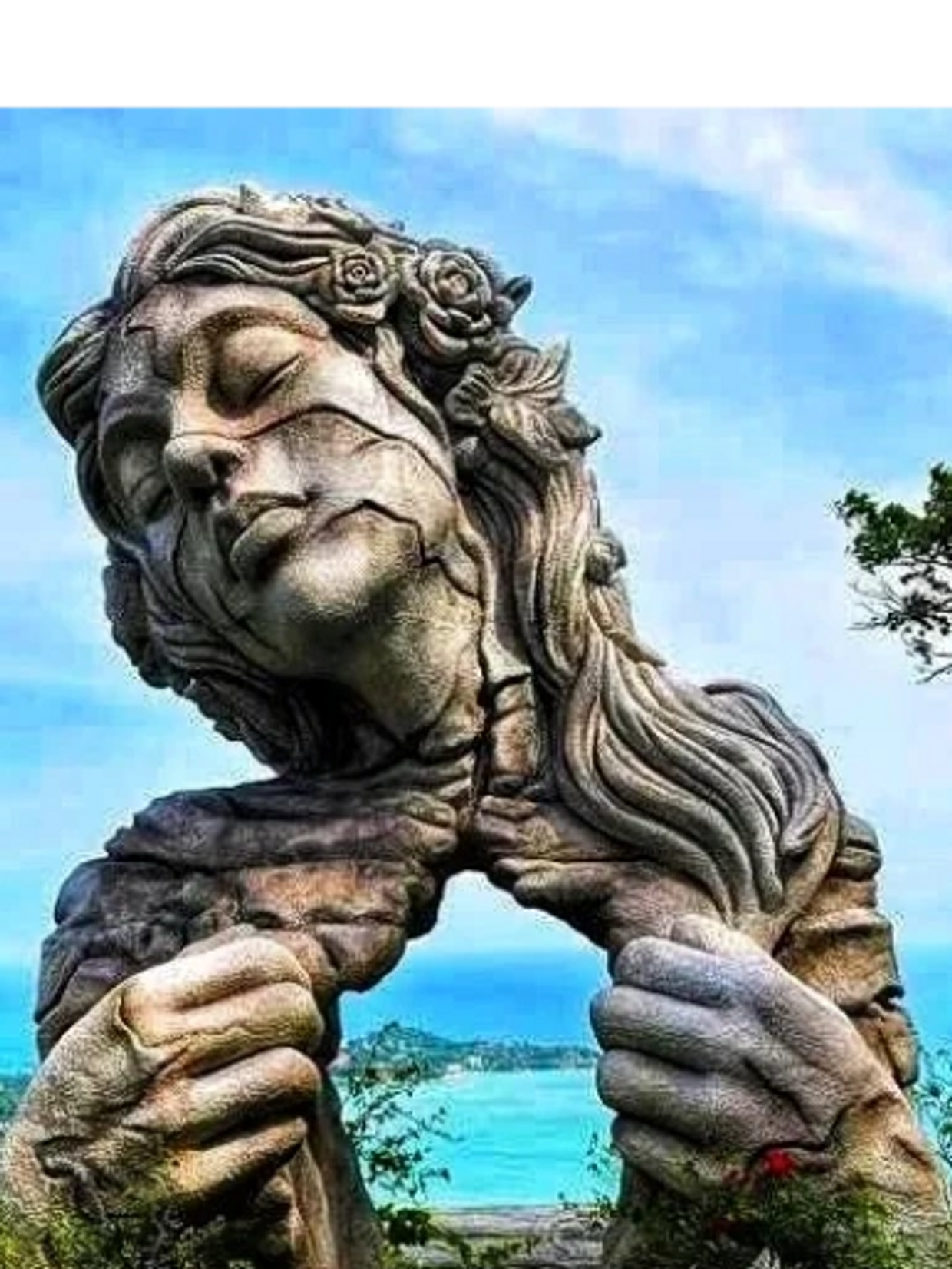 Cracked stone sculpture of a woman tearing open her chest by the sea.