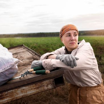 A woman farmer resting on a truck bed in a field at sunset.