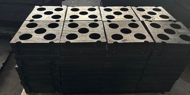 Stacked industrial metal molds with circular holes on a wooden pallet.
