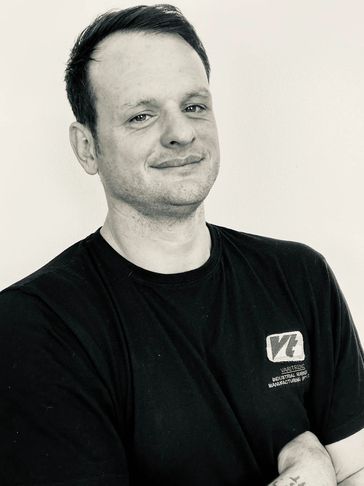 Confident man in black t-shirt with crossed arms, smiling slightly.