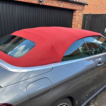 Gray convertible car with a red soft top roof parked by a black garage door.