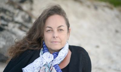 Woman with a scarf outdoors by rocks and sand.