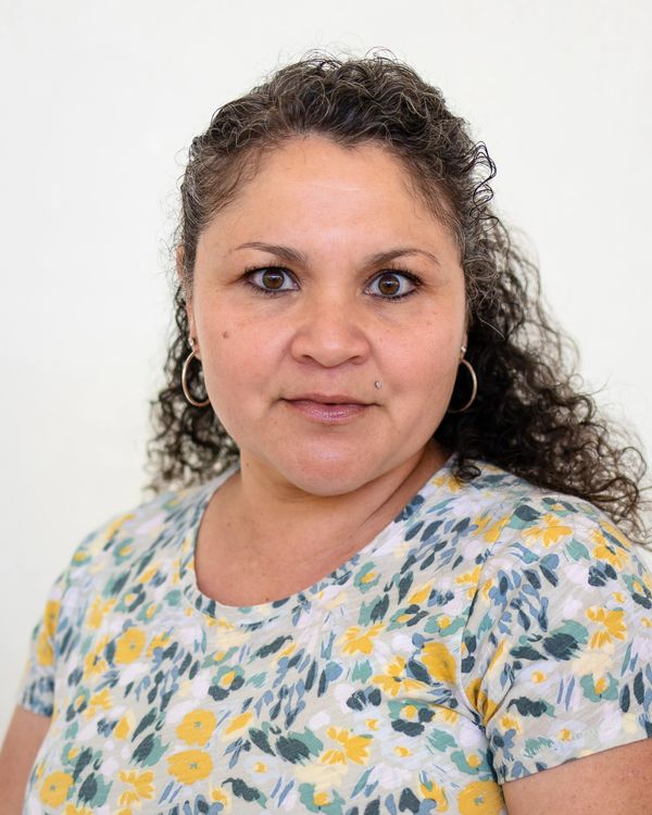 Confident woman with curly hair wearing a floral shirt, looking directly at the camera.