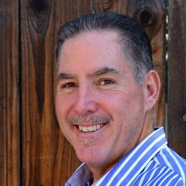 Smiling man with a mustache in a striped shirt against a wooden background.