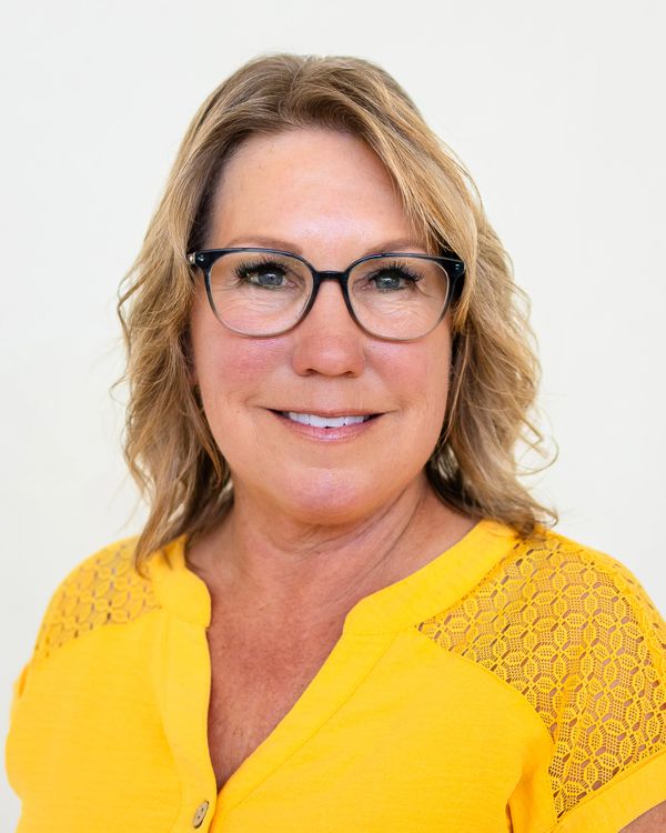 Smiling woman wearing glasses and a bright yellow top.